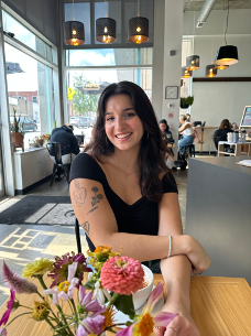 Briana Bindus, white woman with long brown hair, sitting in a cafe