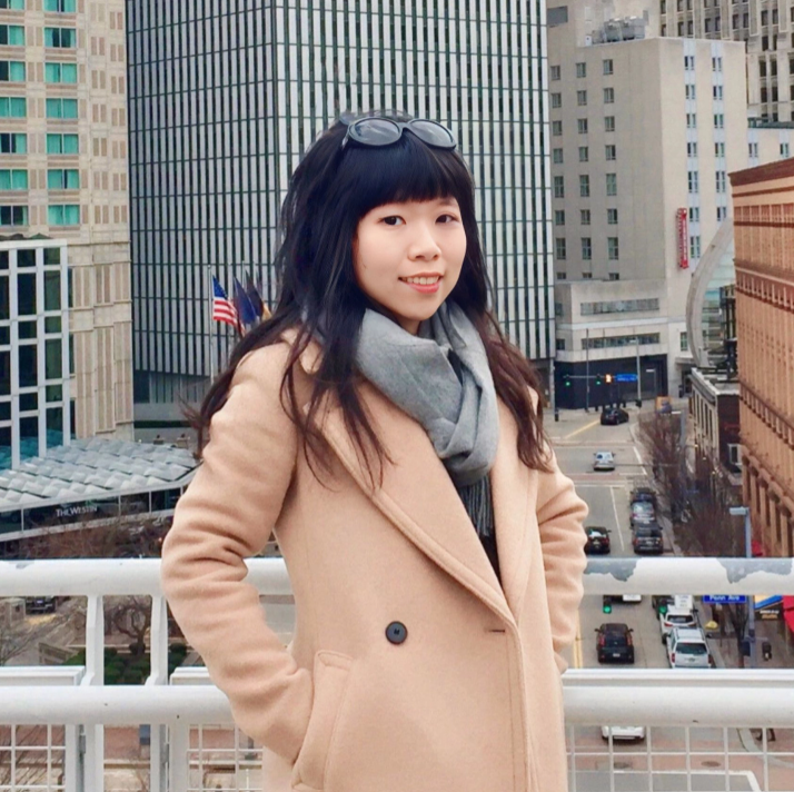 Jialei Jiang stands on a city rooftop. She has light skin and dark shoulder-length hair with glasses on the top of her head.