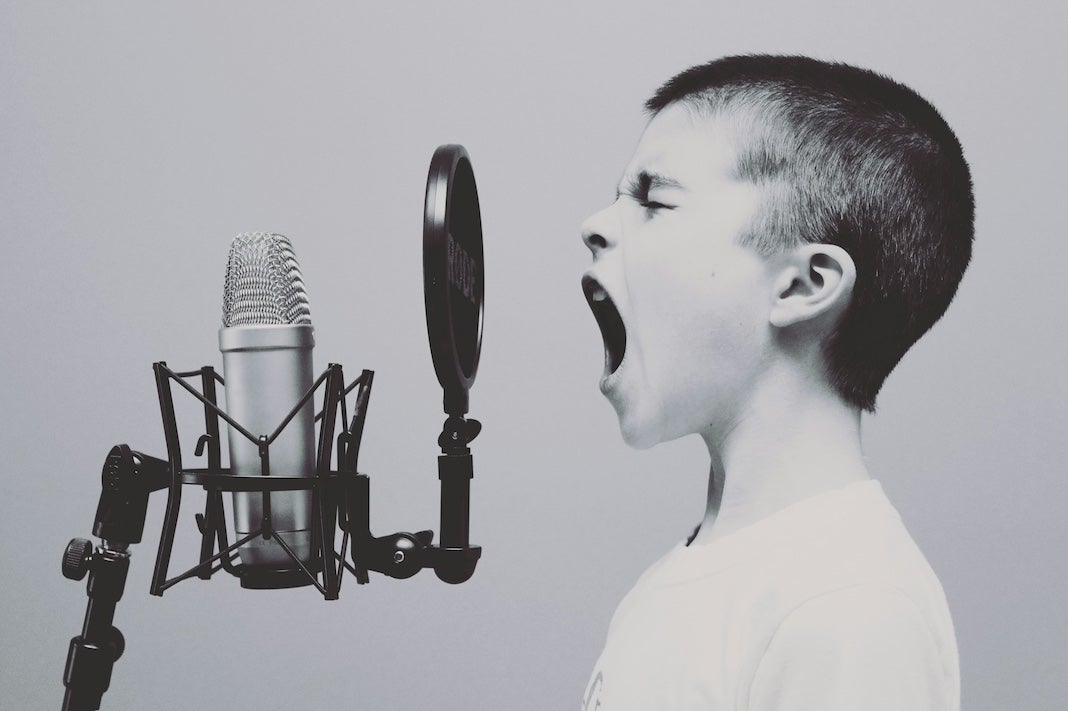 Black and white photo of a young white boy with short brown hair in profile, speaking into an old-fashioned mic