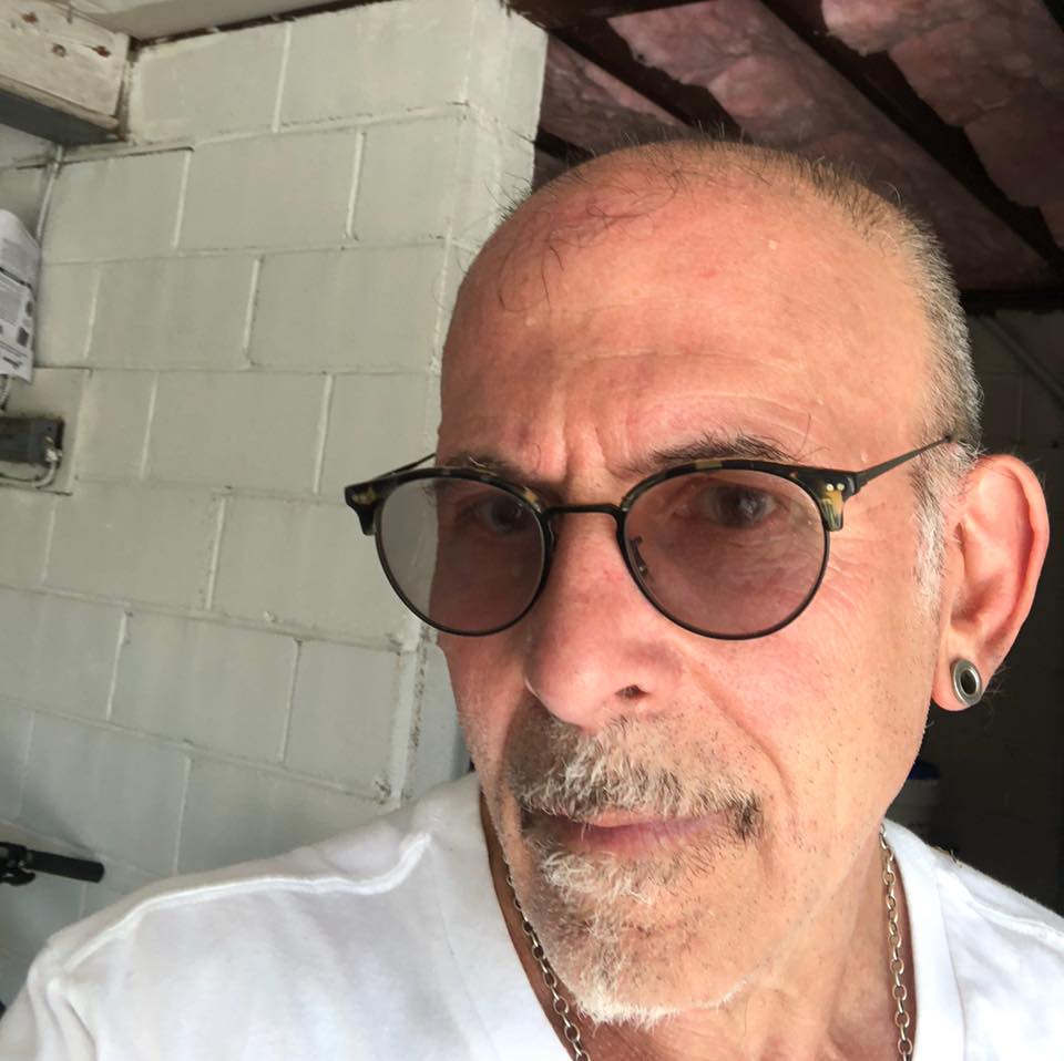 Peter Trachtenberg, light skin close shaved head, beard, tinted glasses.